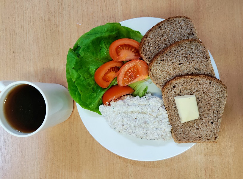 Na zdjęciu znajduje się: Herbata czarna ekspresowa z cytryną Cateringowa, Chleb Graham, Masło extra 82%, Pasta z twarogu i makreli wędzonej, Sałata zielona, Pomidor